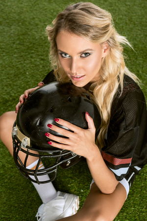high angle view of young woman in american football uniform holding helmet and looking at cameraの写真素材