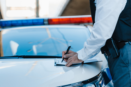 cropped image of male police officer writing in clipboard on car at streetの写真素材