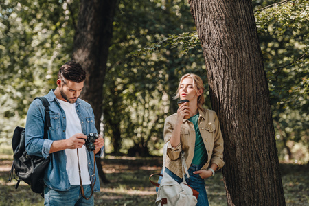 portrait of pensive woman with coffee to go and man with photo camera in parkの写真素材