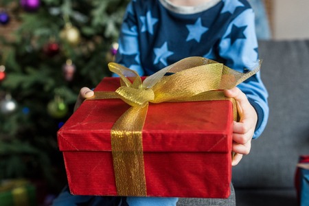 close-up partial view of child in pajamas sitting on couch and holding christmas present