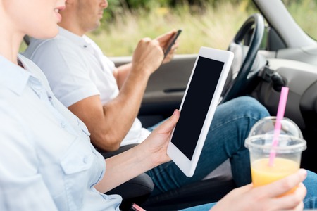 cropped shot of woman with plastic cup of orange juice using tablet in car while man using smartphone on backgroundの写真素材