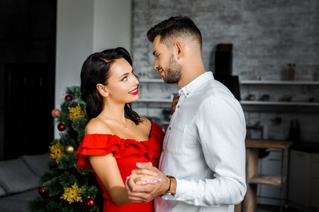 side view of happy young couple looking at each other and dancing on christmas at homeの写真素材