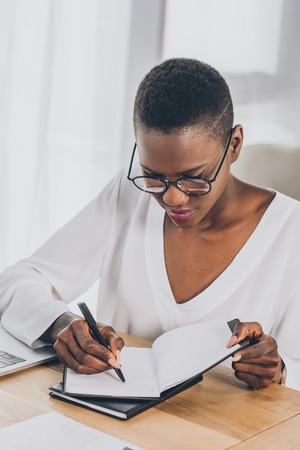 stylish attractive african american businesswoman writing something to notebook in officeの写真素材