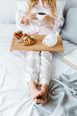 cropped image of woman in pajamas having breakfast in bed in morningの写真素材