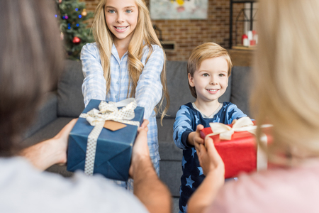 cropped shot of parents presenting christmas gifts to happy kids in pajamasの写真素材