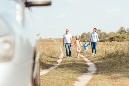 beautiful young family holding hands and walking to car by fieldの写真素材