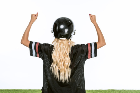 rear view of woman in american football uniform celebrating victory while standing on grass isolated on whiteの写真素材