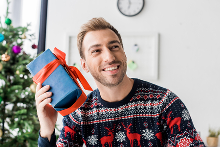 smiling man in christmas sweater with present near headの写真素材