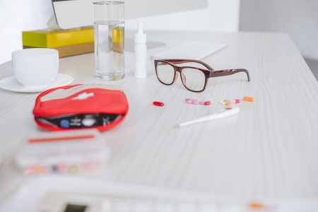 first aid kit, pills, glasses and glass of water on table in officeの写真素材