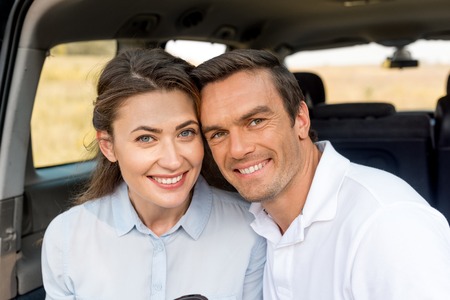 close-up portrait of happy adult couple looking at camera while sitting in car trunk