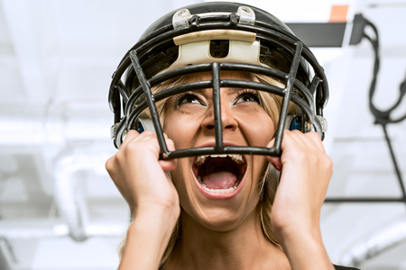 bottom view of mad young woman screaming and holding american football helmet on head