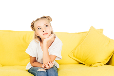 pensive adorable child sitting on yellow sofa and looking up isolated on whiteの写真素材