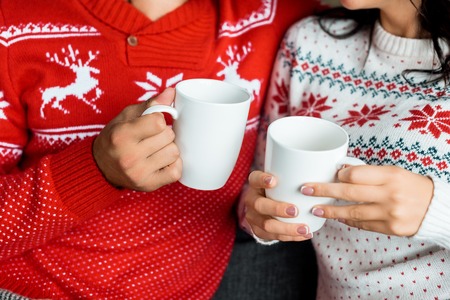 cropped image of couple holding hot coffee cups on sofa at homeの写真素材