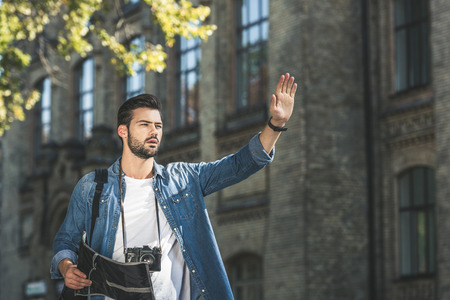 portrait of young tourist with map and photo camera calling taxi on streetの写真素材