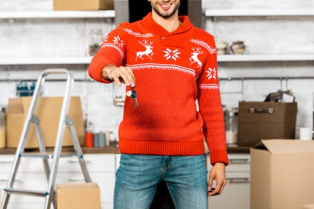 partial view of young man showing keys in kitchen with cardboard boxes during relocation in new homeの写真素材