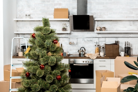 interior of kitchen with decorated christmas tree and cardboard boxes during relocation at new homeの写真素材