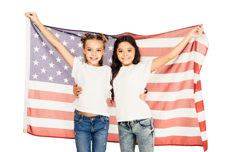 cheerful adorable kids standing under american flag and looking at camera isolated on whiteの写真素材