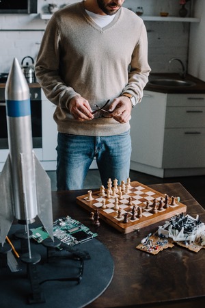 cropped image of man standing near table with chess board at homeの写真素材