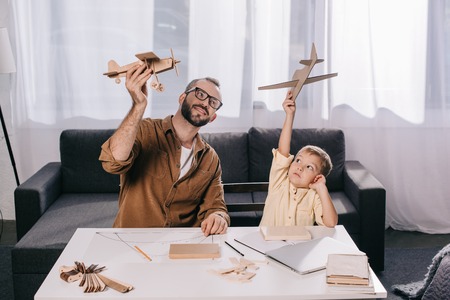happy father and son holding toy planes while modeling together at homeの写真素材