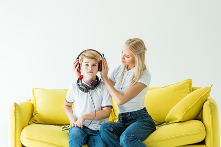 mother wearing headphones on son on yellow sofa isolated on whiteの写真素材