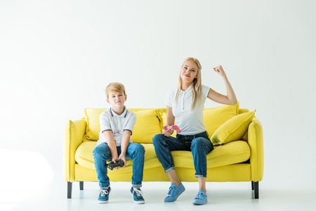 happy mother showing yes gesture after winning video game on yellow sofa on whiteの写真素材