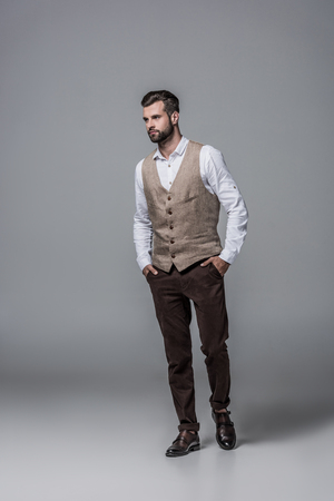 handsome bearded man posing in trendy elegant waistcoat on greyの写真素材