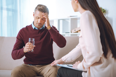 male patient with glass of water having therapy appointment at psychologist officeの写真素材