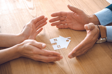 partial view of insurance agents and female hands with paper house model on wooden tabletop, house insurance conceptの写真素材