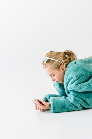 stylish kid in turquoise fur coat using smartphone isolated on whiteの写真素材