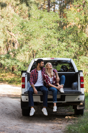 couple hugging and sitting together on pickup truck in forestの写真素材