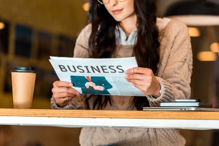cropped view of woman reading business newspaper at cafe with coffee to goの写真素材