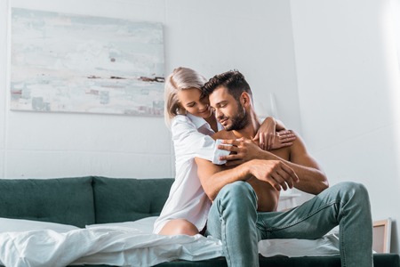 attractive young woman embracing her boyfriend from behind in bedroomの写真素材