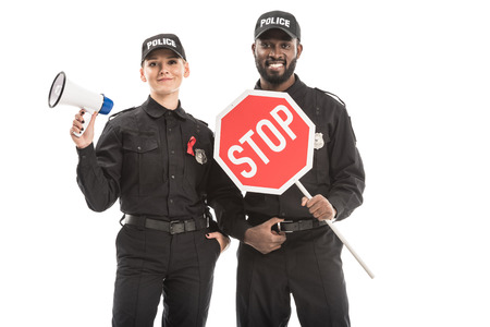 smiling police officers with stop road sign and megaphone looking at camera isolated on white, aids...