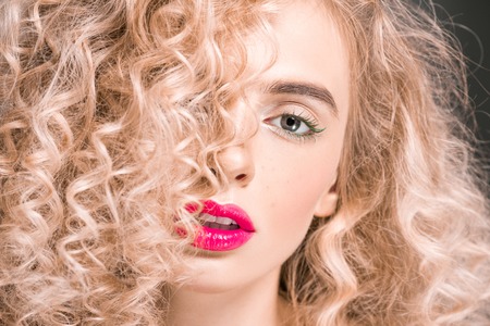 attractive girl with long curly hair looking at camera on greyの写真素材