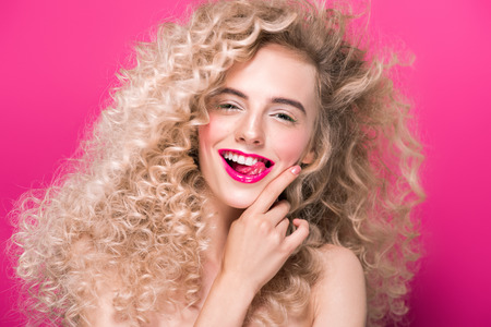 portrait of beautiful young woman with long curly hair smiling at camera isolated on pinkの写真素材