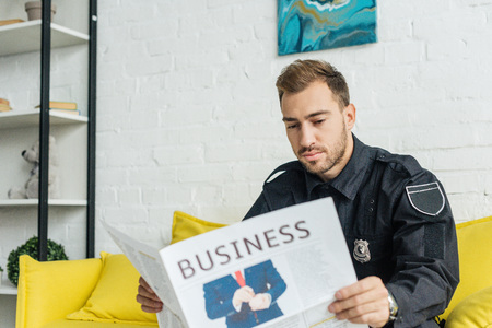 attractive young policeman reading newspaper on couchの写真素材