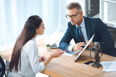 male lawyer pointing at clipboard and looking at client in officeの写真素材