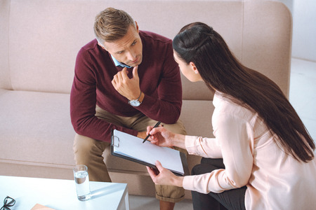 female psychologist pointing at blank clipboard during therapy appointment with male patientの写真素材