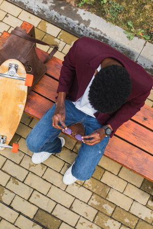 overhead view of young man with eyeglasses and skateboard sitting on benchの写真素材