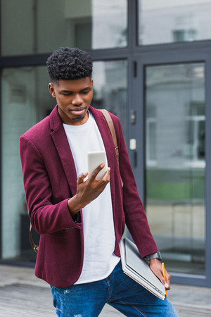 handsome young student with notebooks and smartphone standing on streetの写真素材