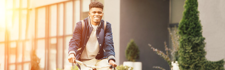 cheerful african american man riding bicycle in city with sunlightの写真素材