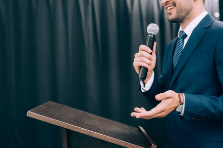 cropped image of speaker gesturing and talking into microphone at podium tribune during seminar in conference hallの写真素材