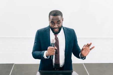 high angle view of smiling african american speaker talking into microphone during seminar in conference hallの写真素材