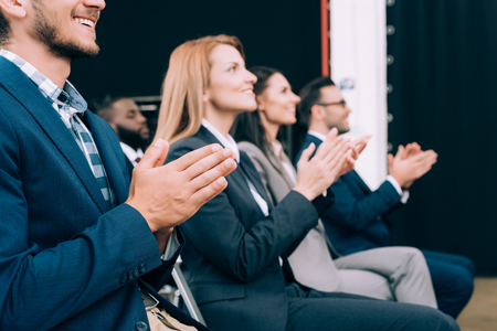 smiling multicultural businesspeople applauding during business seminar in conference hallの写真素材