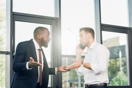 african american businessman looking at colleague talking on smartphone in conference hallの写真素材