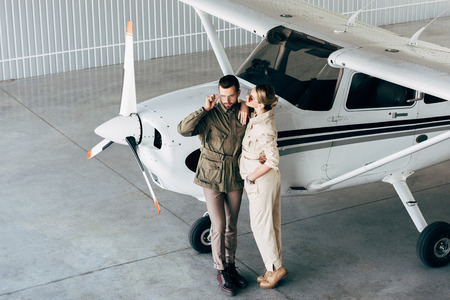 high angle view of fashionable young couple in stylish jackets standing near airplane in hangarの写真素材