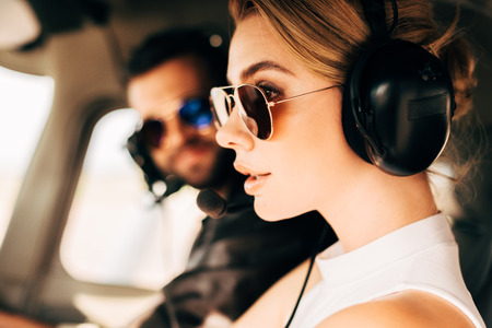 side view of attractive woman in sunglasses and headset sitting near male pilot in cabin of airplaneの写真素材