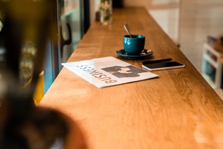 smartphone, business newspaper and cup of tea on table in cafeの写真素材