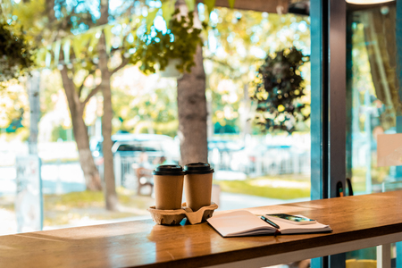 two coffee in paper cups, open notebook with pen on cafe counterの写真素材