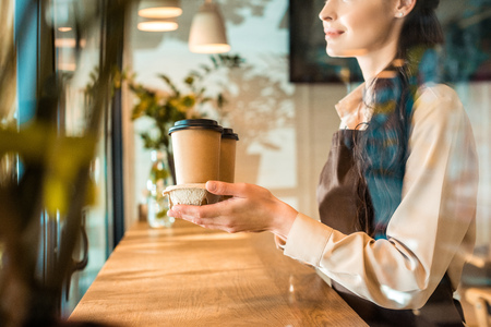 cropped image of waitress in apron holding coffee in paper cups in cafeの写真素材